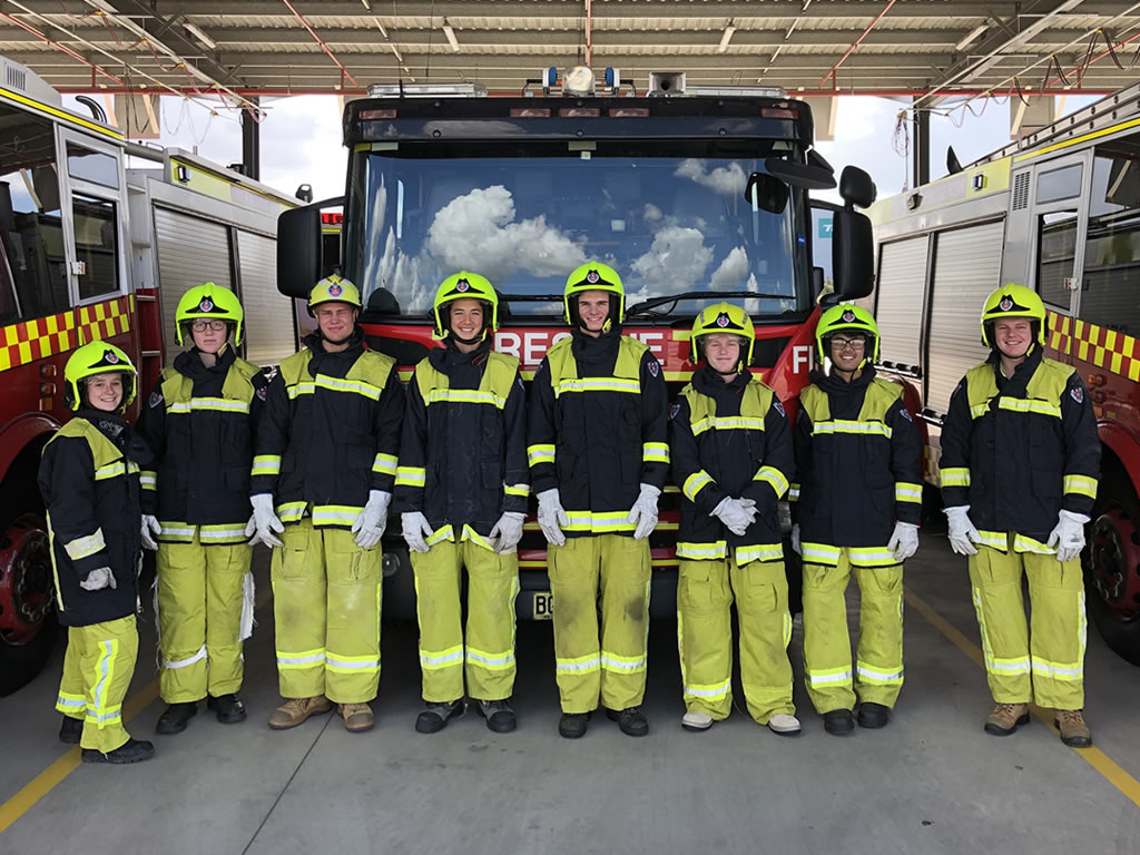 Photo of students wearing firefighting gear,  standing in front of a fire truck.